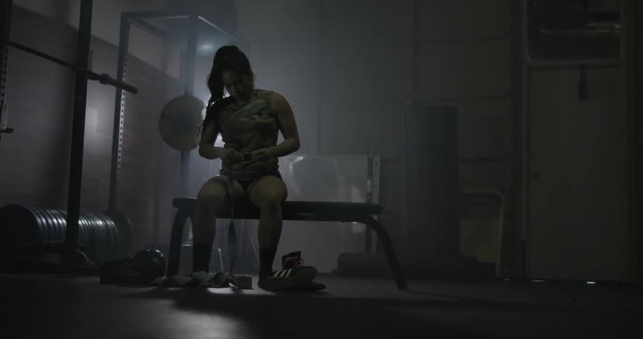 A woman picks up athletic tape from the ground while sitting in a weight room