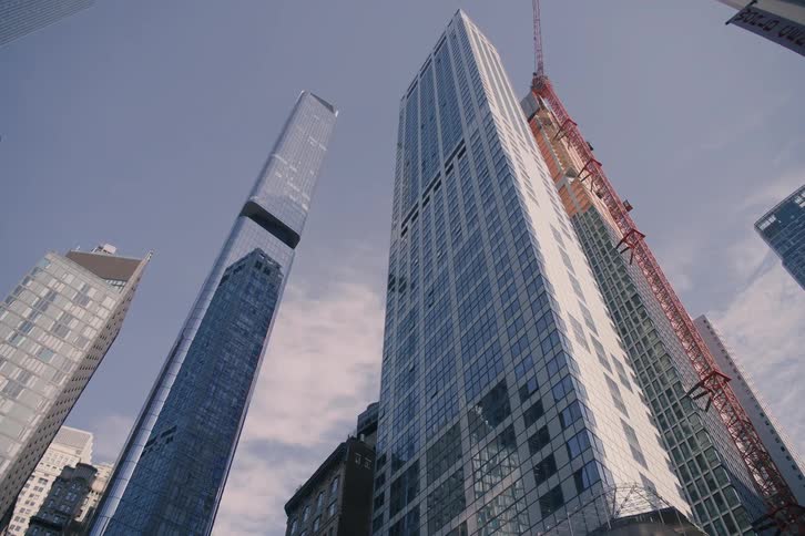 Looking up from street level at the impressive architecture of towering glass skyscrapers in a modern city, with one building under construction