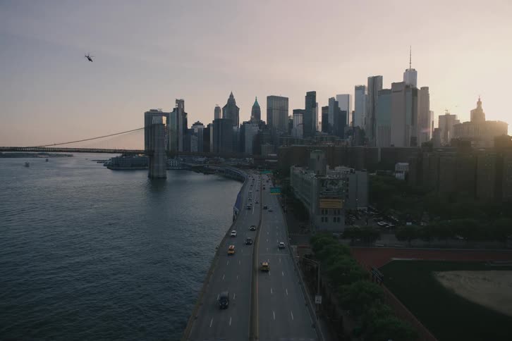 Slow push-in shot through a chain-link fence reveals the FDR Drive and the Lower Manhattan skyline at sunset