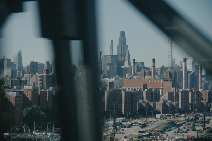 Dynamic parallax view of the New York City skyline and a waterfront construction site, filmed from a moving vehicle crossing a bridge