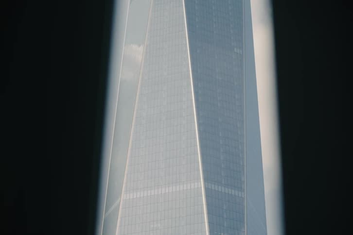 A slow upward tilt reveals the iconic spire of the One World Trade Center, framed by a silhouetted window