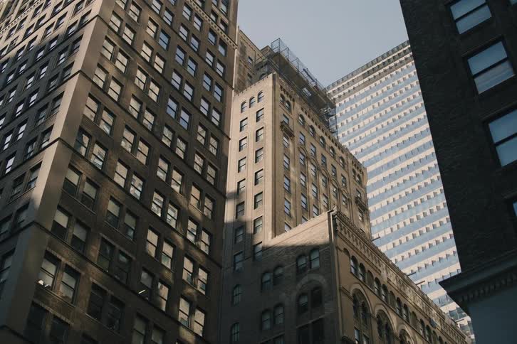 A low-angle tracking shot reveals the classic and modern architecture of towering skyscrapers in a downtown city on a sunny day