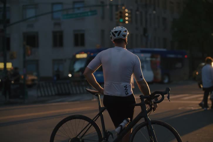A cyclist stands with his bicycle at a city intersection waiting for pedestrians to cross during a beautiful golden hour sunset