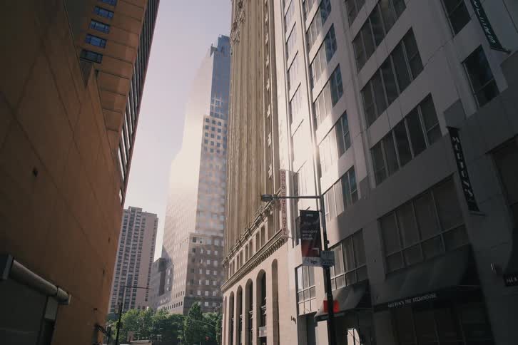 A slow-motion dolly shot pulls back from under an awning to reveal a sunlit city alleyway surrounded by tall buildings
