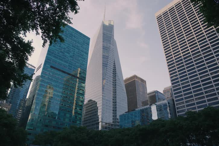 A slow pull-back from a low angle reveals towering modern glass skyscrapers from a park at dusk