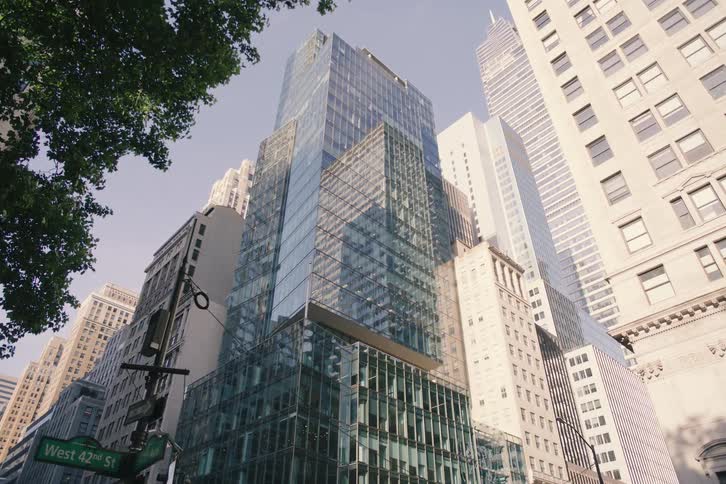 A slow pull-back shot from under a tree reveals the towering modern skyscrapers on West 42nd Street in New York City