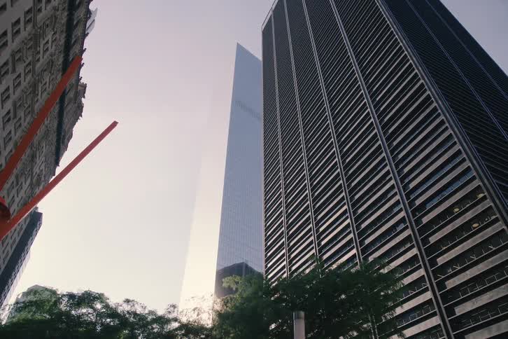 A slow revealing low angle shot looks up at the towering skyscrapers on Broadway in New York City as the bright sun flares between them