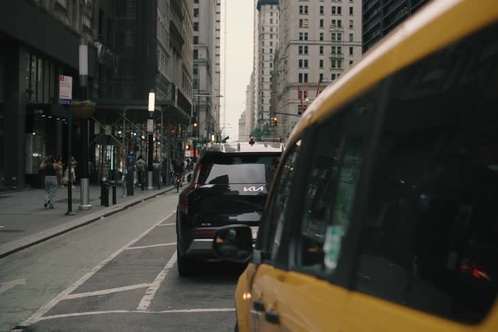 A young woman gets into a yellow NYC taxi on a busy street, which then slowly pulls forward into traffic