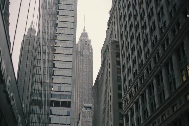 A slow reveal of a classic art-deco skyscraper standing tall amongst modern buildings in New York City on an overcast day