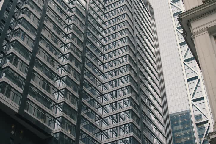 Low angle shot tilting up a modern, geometric skyscraper next to a classic architectural building in a dense city