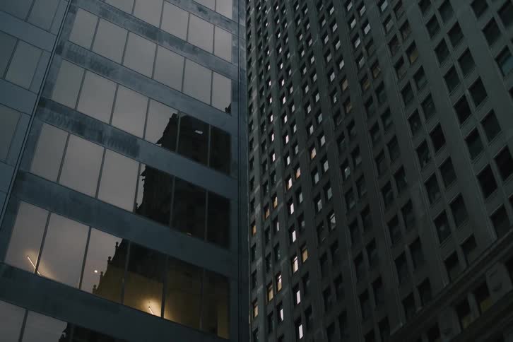 A slow pull-back shot reveals contrasting architecture between a modern glass skyscraper and an older city building at dusk