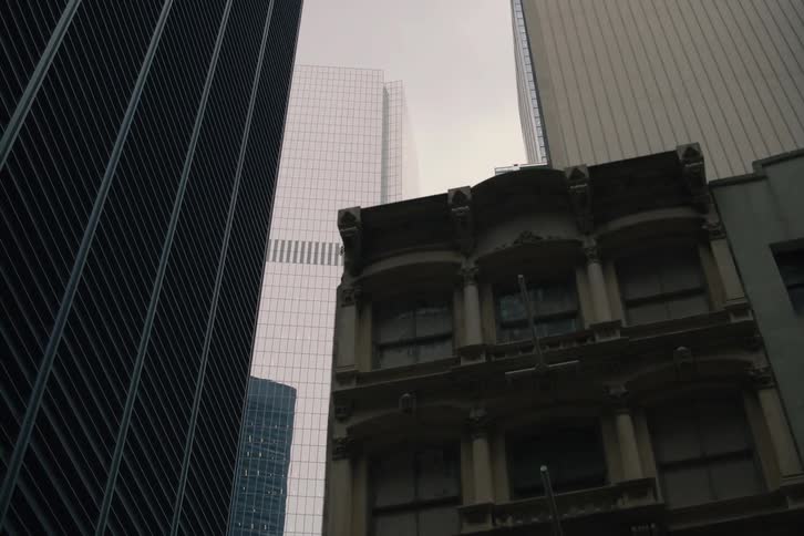 A slow dolly shot reveals a modern skyscraper towering behind older buildings on a gloomy day in a dense city