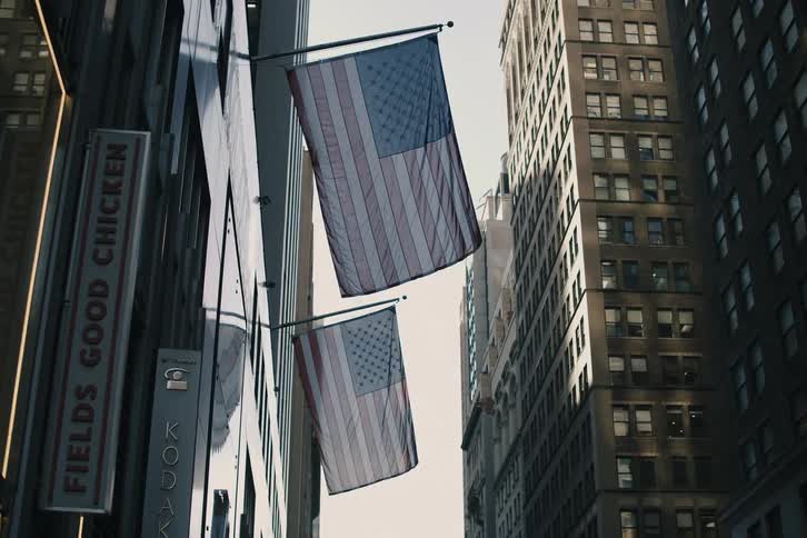 A slow zoom on two American flags hanging between tall skyscrapers in a dense urban city