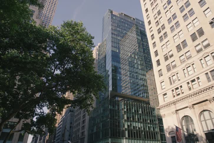 A slow, upward-looking glide through a canyon of New York City skyscrapers, with sunlight illuminating their grand architecture