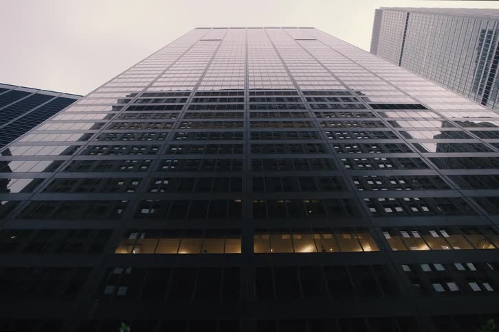 A slow pull-back from a low-angle shot of a towering glass skyscraper in a modern city