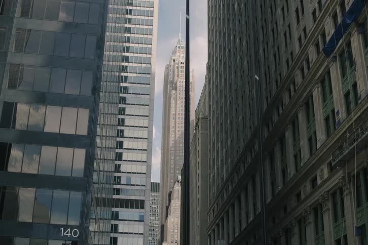 A slow reveal of a classic skyscraper framed by modern office buildings on a downtown city street