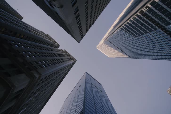 A slow pull-back from a low-angle perspective reveals four towering skyscrapers reaching for the clear sky