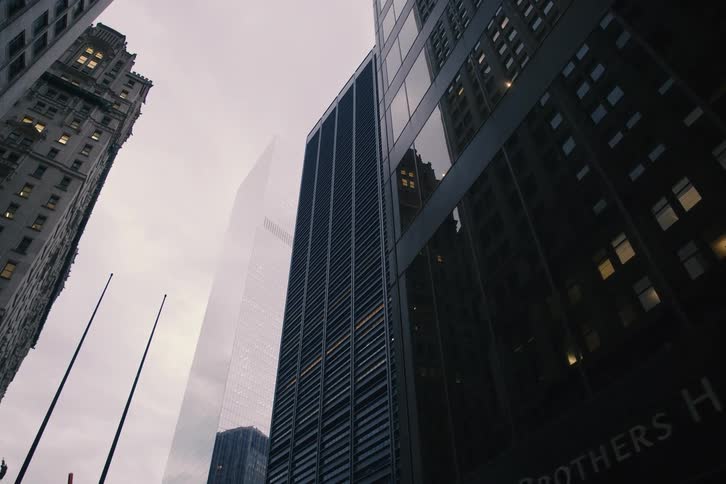 A slow upward tilt reveals the impressive architecture of towering skyscrapers in a downtown financial district on a cloudy day
