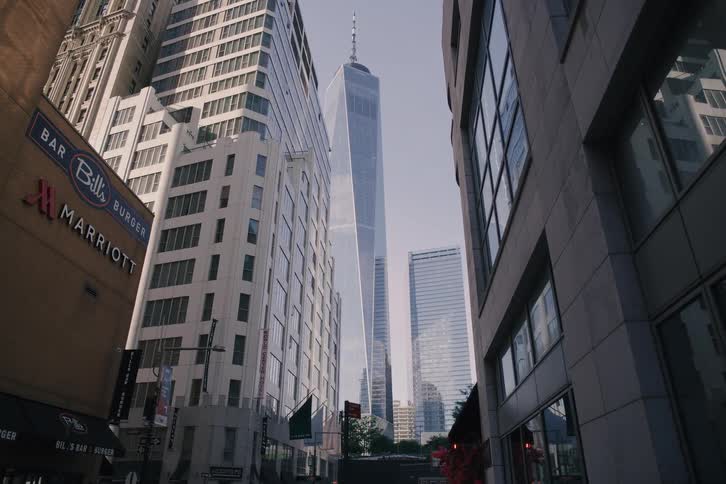 A slow, low-angle dolly shot moves forward down a city street towards the towering One World Trade Center in Manhattan