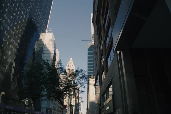 A slow push-in shot looking up a sunlit street canyon surrounded by modern skyscrapers in New York City