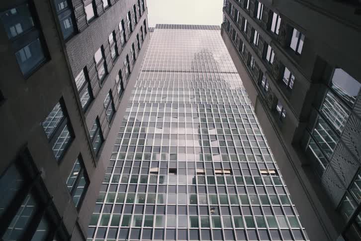 A slow pull-out from a low-angle shot reveals a towering glass skyscraper framed by older buildings on a city street