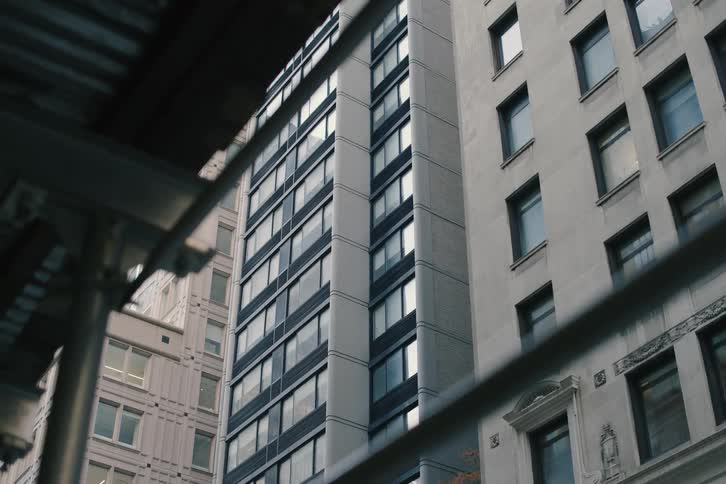 A slow dolly shot from behind scaffolding reveals the towering facades of city buildings on an overcast day