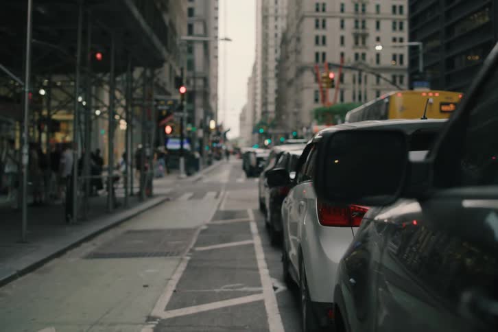 Observational slow dolly shot along a line of parked cars on a busy street in New York City