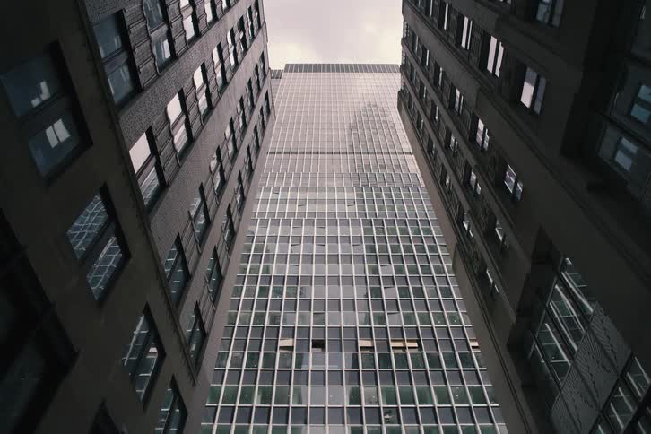 A slow pull-back from a low-angle shot of a modern glass skyscraper framed by two imposing older buildings
