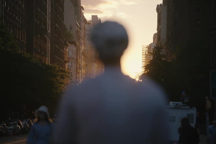 A focus pull shot reveals a beautiful city sunset behind a cyclist standing on a busy street