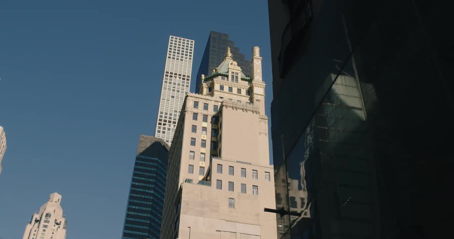 A slow dolly shot pulls back from the shadows to reveal classic and modern New York City skyscrapers against a clear blue sky
