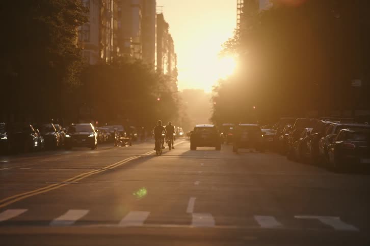 A slow-motion, out-of-focus view of cyclists riding down a busy New York City street during a beautiful golden hour sunset