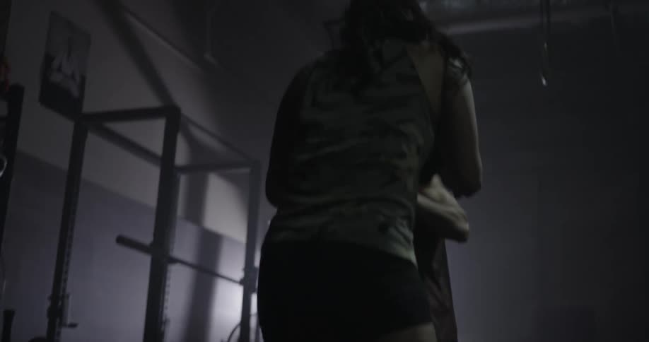 A man and woman dance around sparring in a dark gym