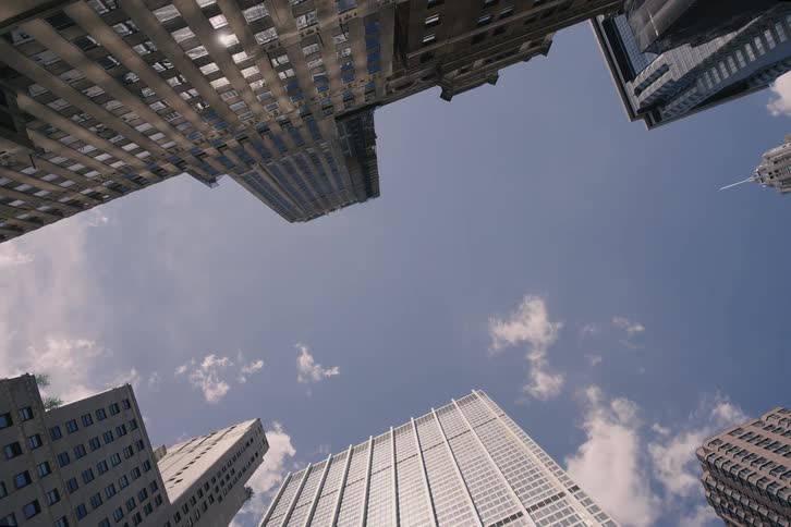 A slow pull-back shot looking straight up at the towering skyscrapers of a modern financial district against a blue sky