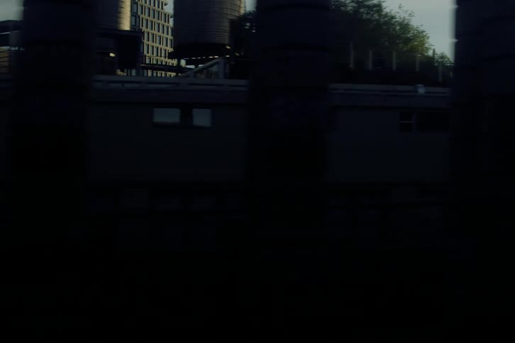 A cinematic slow-motion view of sunlit city buildings as seen from a moving train crossing a bridge during the golden hour