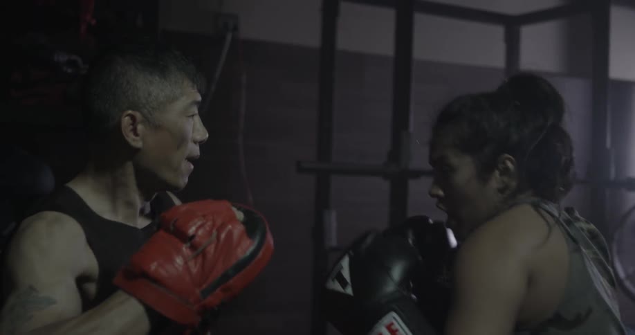 A man lets a woman box his gloves in a gym