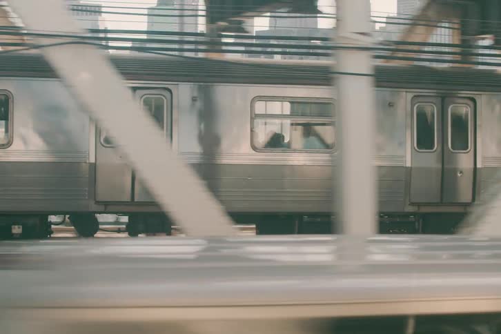 A cinematic tracking shot of a New York City subway train crossing a bridge with the sunlit city skyline in the background