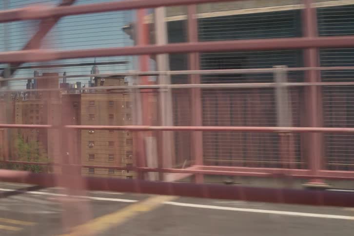 A dynamic tracking shot from a vehicle crossing the Williamsburg Bridge, revealing the New York City skyline and apartment buildings on a sunny day