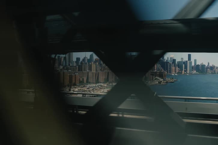Iconic Manhattan skyline seen from a moving train crossing a bridge over the East River on a sunny day