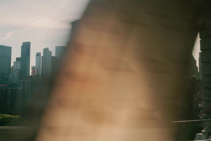 A hazy, sun-drenched view of the New York City skyline as seen from a moving train crossing a bridge