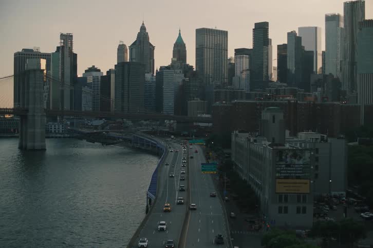 An atmospheric shot of the Lower Manhattan skyline and the Brooklyn Bridge at dusk as traffic moves along the FDR Drive