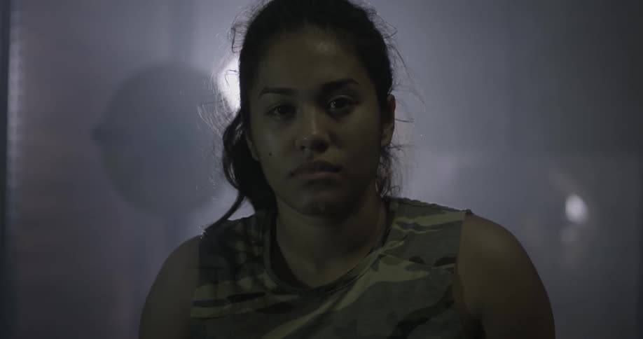 A woman looks forward sitting in a dark gym
