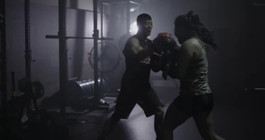Man and woman practice boxing in a dimly lit gym