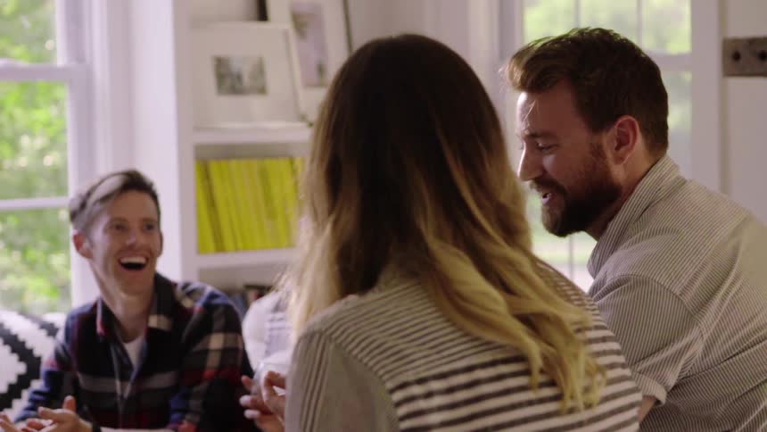 A group of friends laugh and talk as they sit in a living room