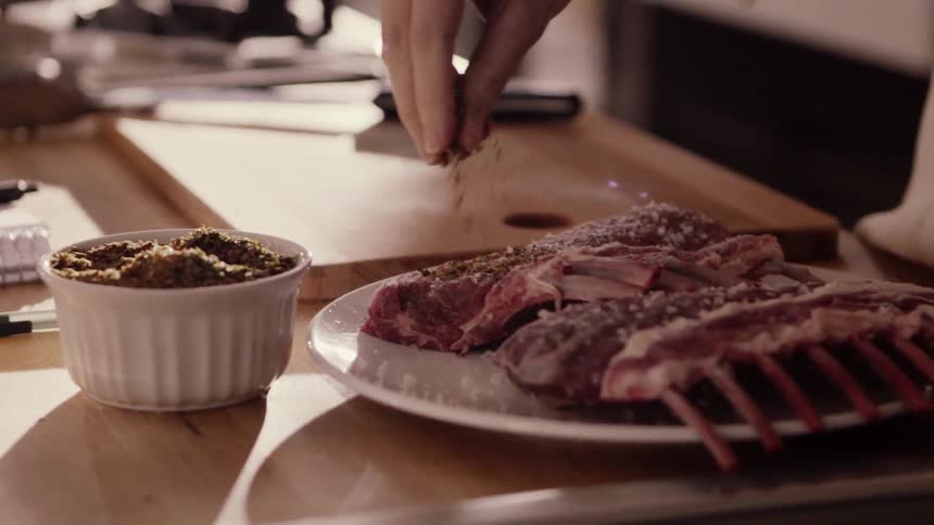 A person sprinkles herbs on some ribs