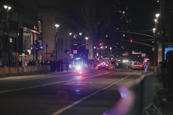 Police secure a city street at night, with a motorcycle and other vehicles flashing their emergency lights