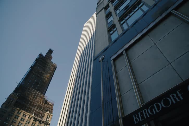 A low-angle timelapse captures the morning sun casting moving shadows across the iconic Bergdorf Goodman building and other skyscrapers in New York City