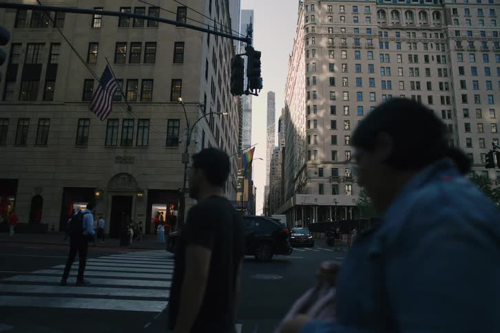 A slow, cinematic pan across a bustling intersection on 5th Avenue in New York City reveals traffic and pedestrians moving between iconic buildings