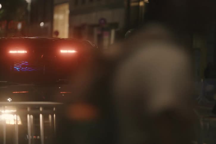 An NYPD officer stands guard by his patrol vehicle with flashing lights as crowds walk by on a city street at night