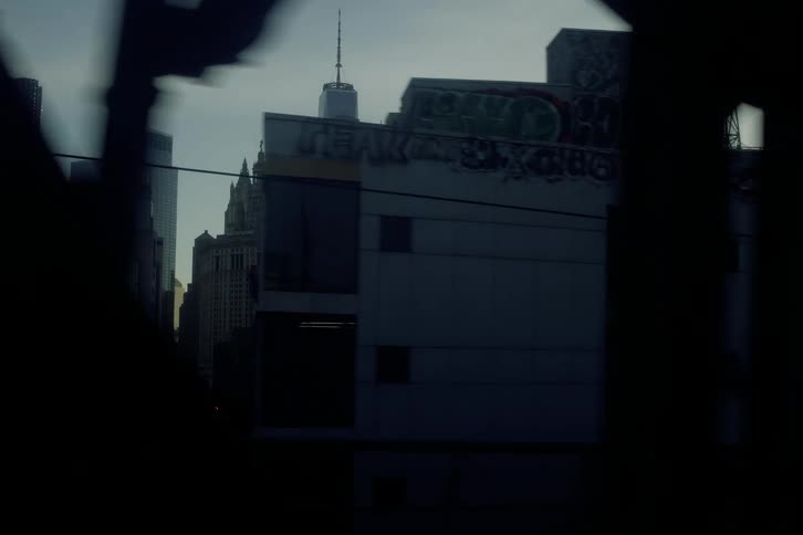A slow-motion view from a train window reveals the moody New York City skyline as the bright sun gives way to twilight