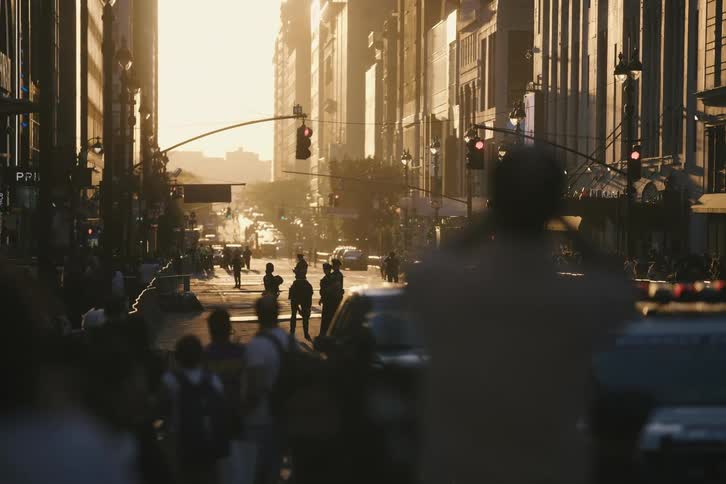 A spectator films a crowded city street with a heavy police presence as the sun sets between the tall buildings